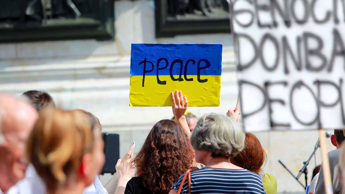 Protesters holding a Ukrainian flag with the word "peace" on it 